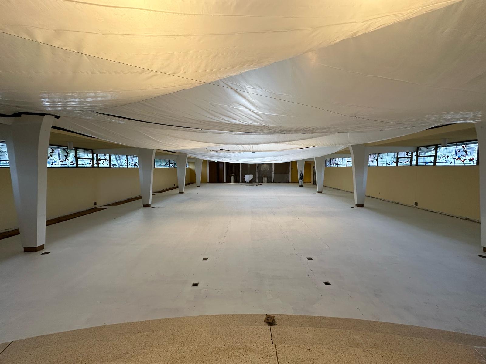 Church sanctuary under renovation with protective sheeting draped over the ceiling and the floor stripped and prepped